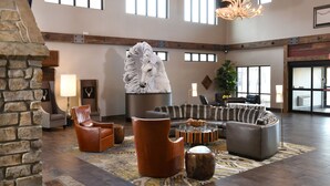 Un hall d’entrée spacieux avec une cheminée en pierre, des fauteuils en cuir et un grand lustre.