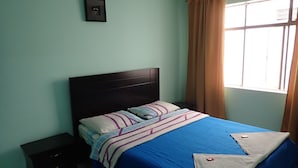 Une chambre avec un lit simple, une table de chevet, une commode et une fenêtre avec des rideaux.