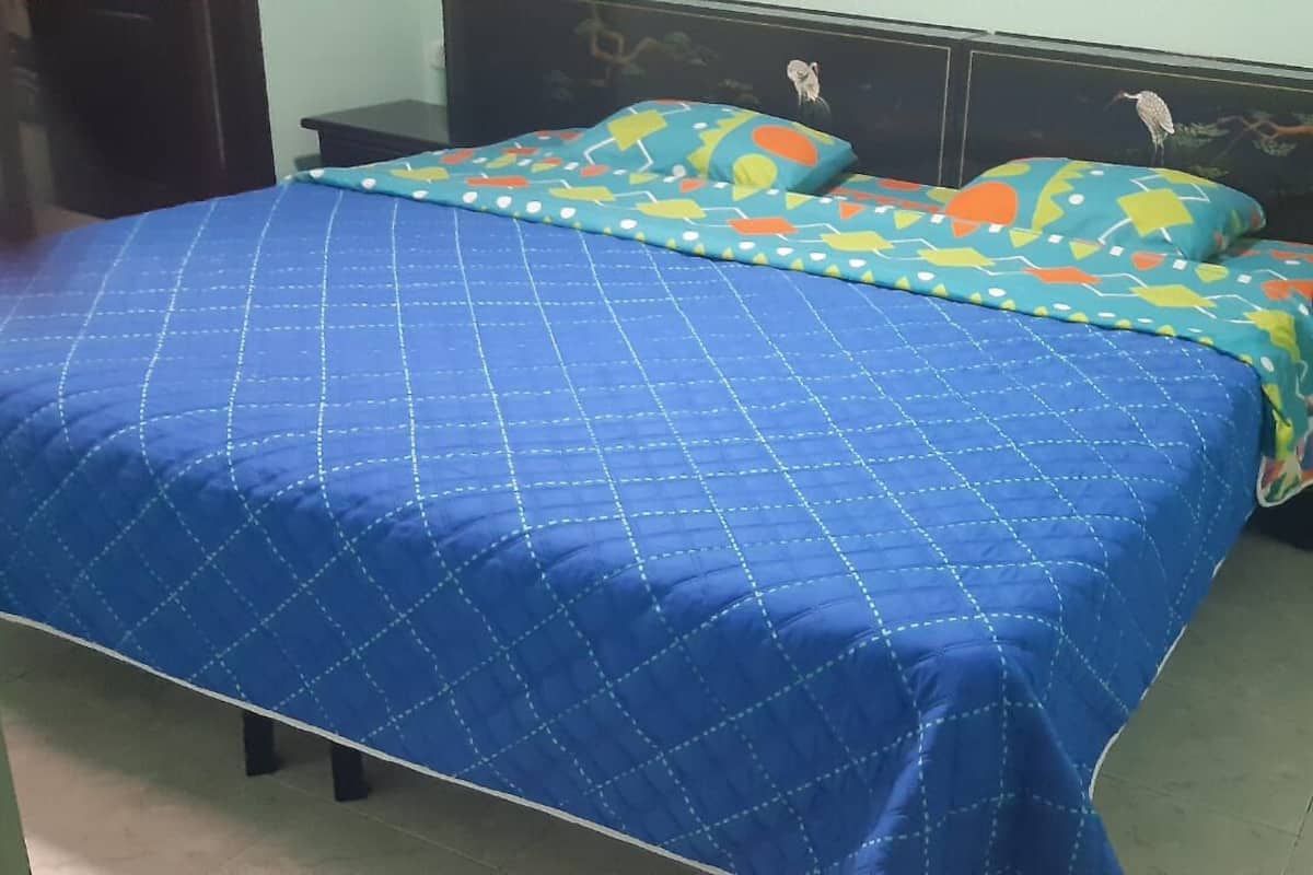 Een bed met een blauwe quilt en kleurrijke kussens, een donker hoofdbord en een betegelde vloer.