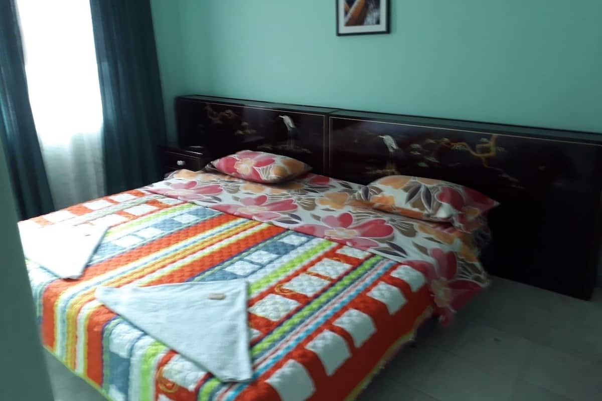 Een bed met een kleurrijke quilt, een donker hoofdbord en een kussen met een bloemenprint.