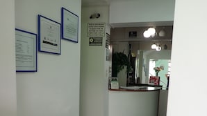 Un couloir orné de cadres contenant des diplômes, un comptoir d’accueil et un sol carrelé.