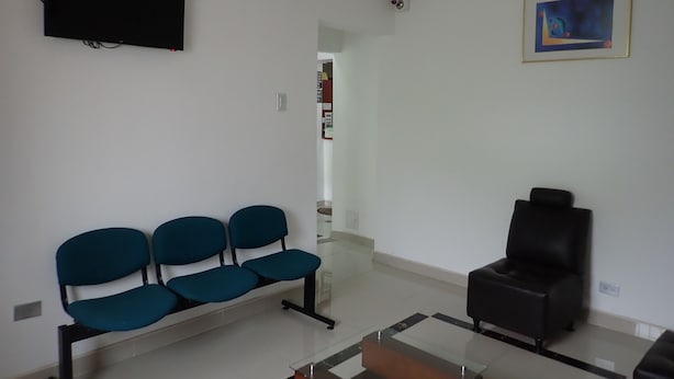 Un salon comprenant un canapé, un fauteuil noir, une table basse en verre et un téléviseur à écran plat fixé au mur.