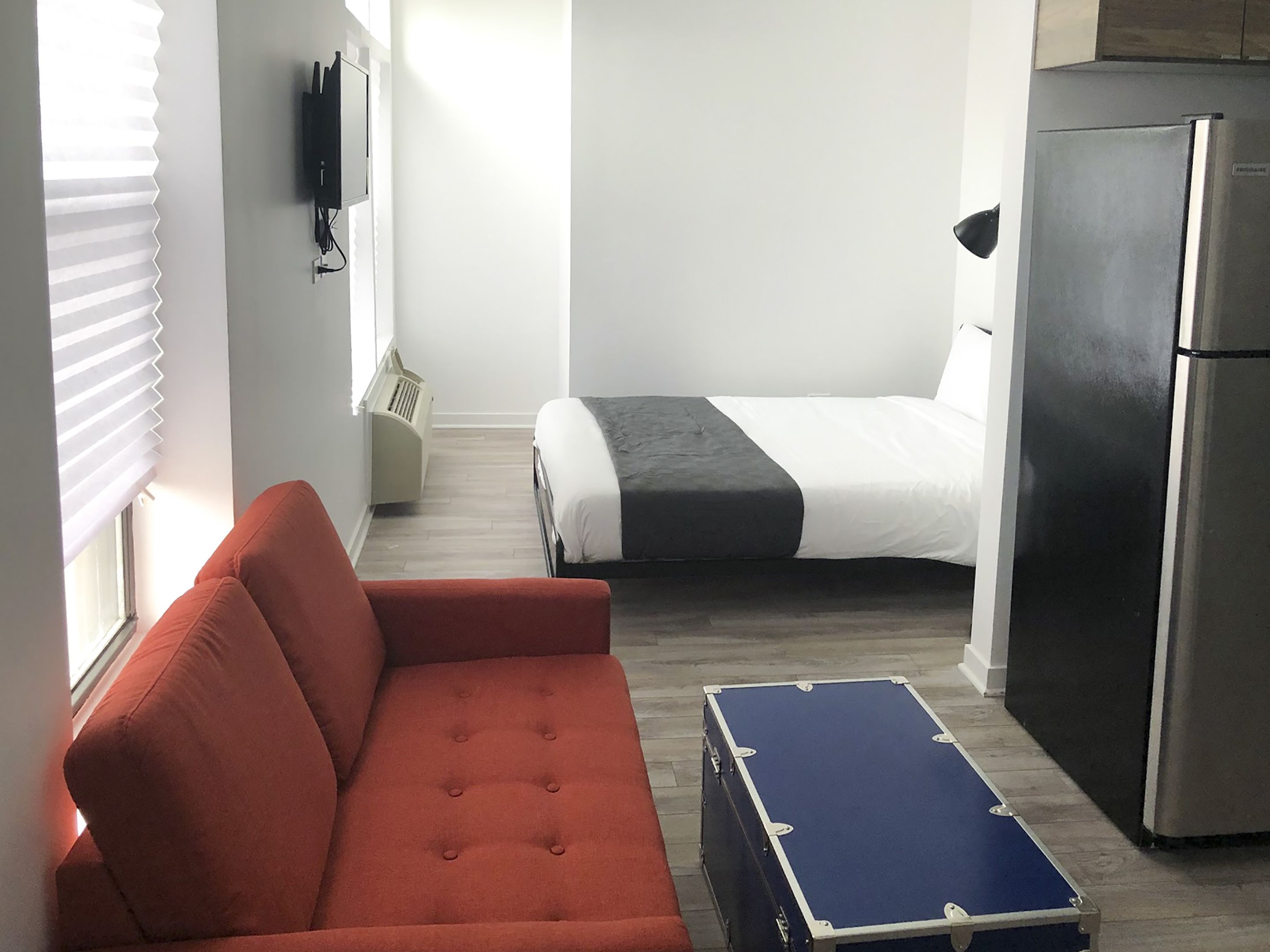 Quarto compacto com sofá, cama, mesinha e geladeira.