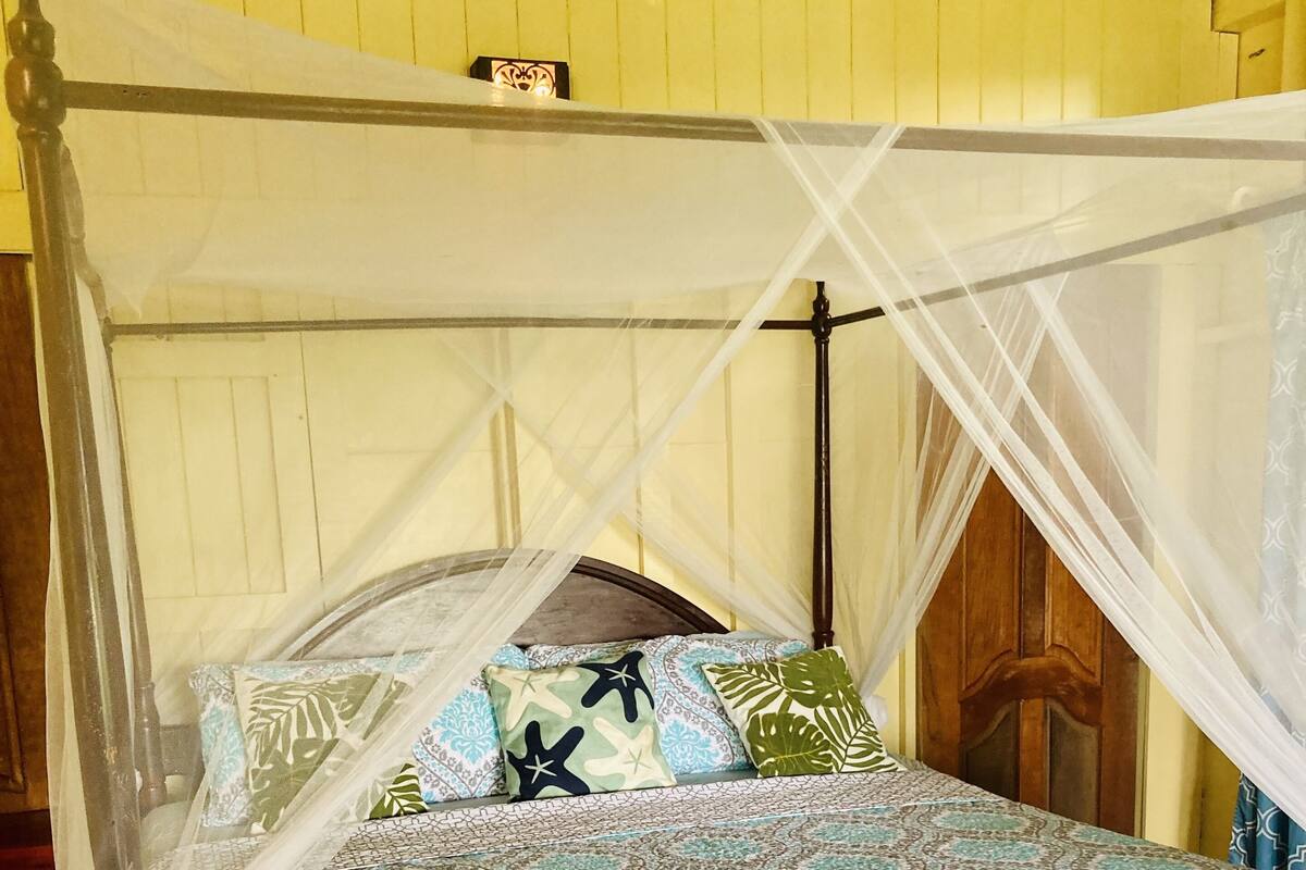 A four-poster bed with a canopy, patterned bedspread, and multiple pillows.