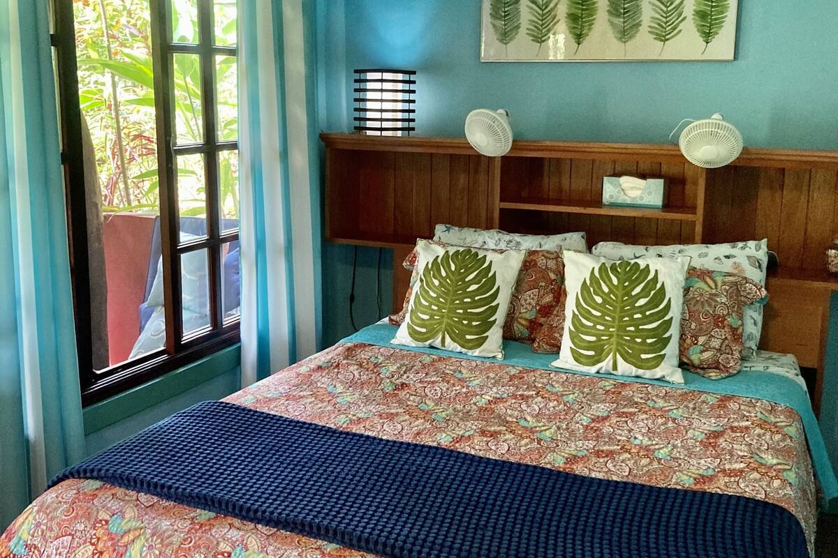 A bedroom with a bed, a ceiling fan, a window with curtains, and a wall-mounted plant.
