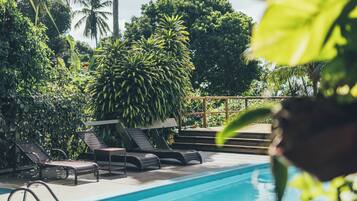 Piscina com espreguiçadeiras, rodeada por vegetação tropical.