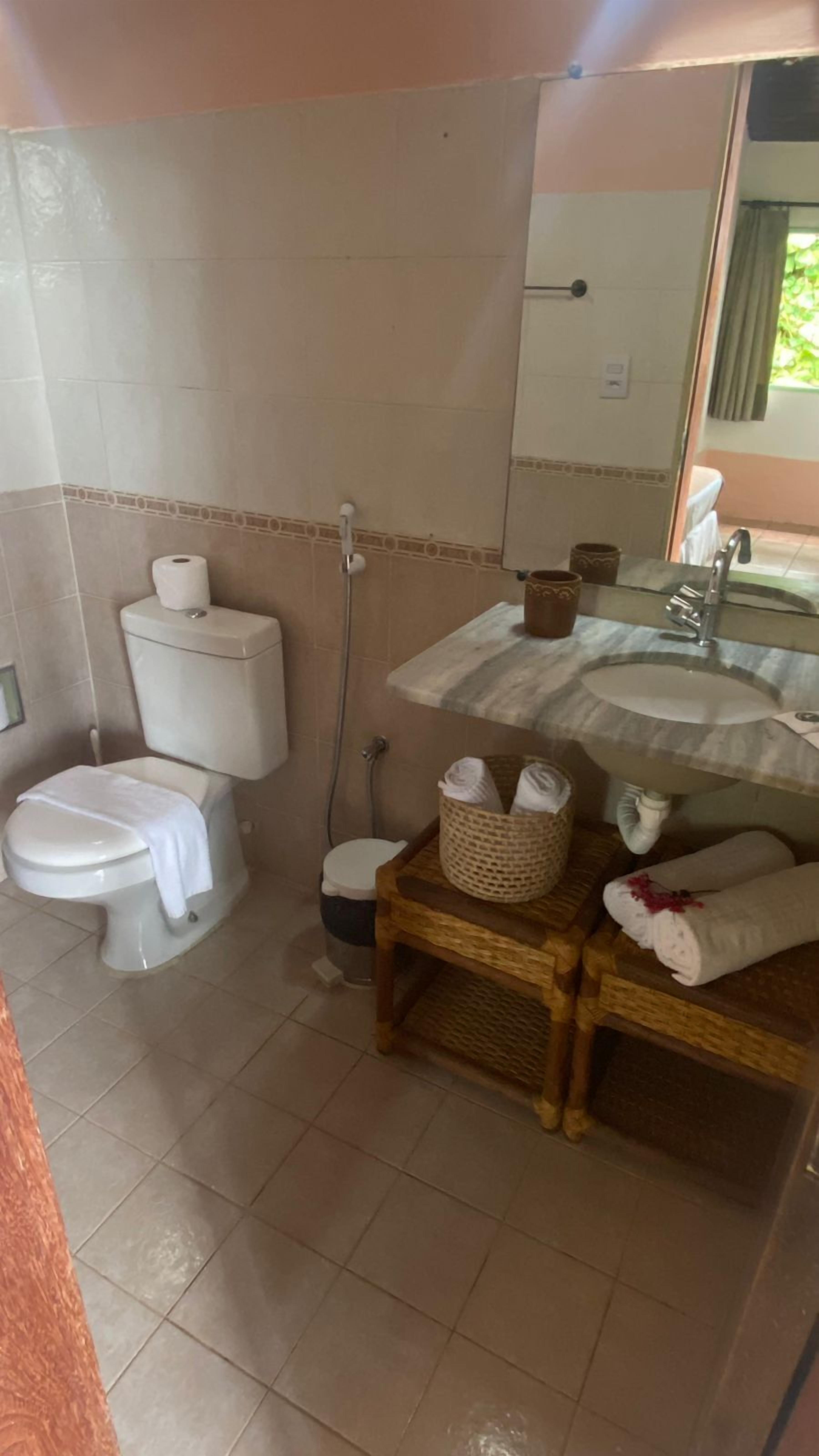 Casa de banho com sanita, bidé, lavatório e uma pequena cesta de vime sobre um banquinho de madeira.