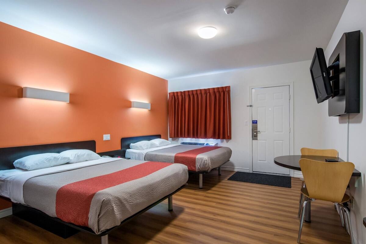Quarto de hotel com duas camas, uma televisão, uma mesa pequena e uma cadeira.