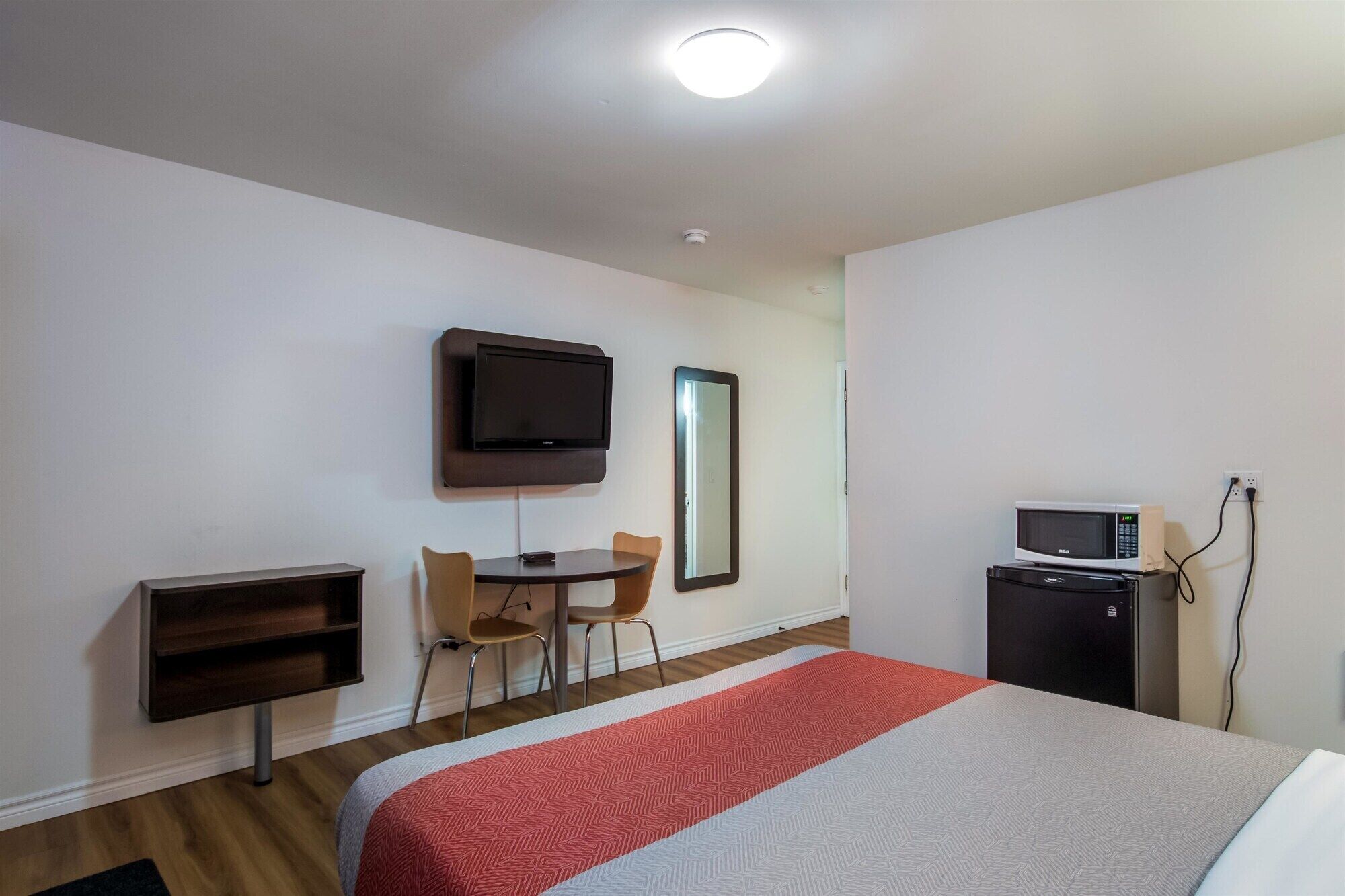 A hotel room with a bed, a desk, a chair, a television, a mirror, and a microwave.