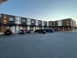 Un edificio moderno con varias unidades, un estacionamiento y varios vehículos, incluyendo motocicletas y un automóvil.
