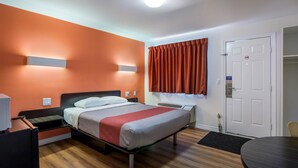 Ein Hotelzimmer mit Bett, Schreibtisch, Stuhl, Tür und einem Fenster mit Vorhängen.