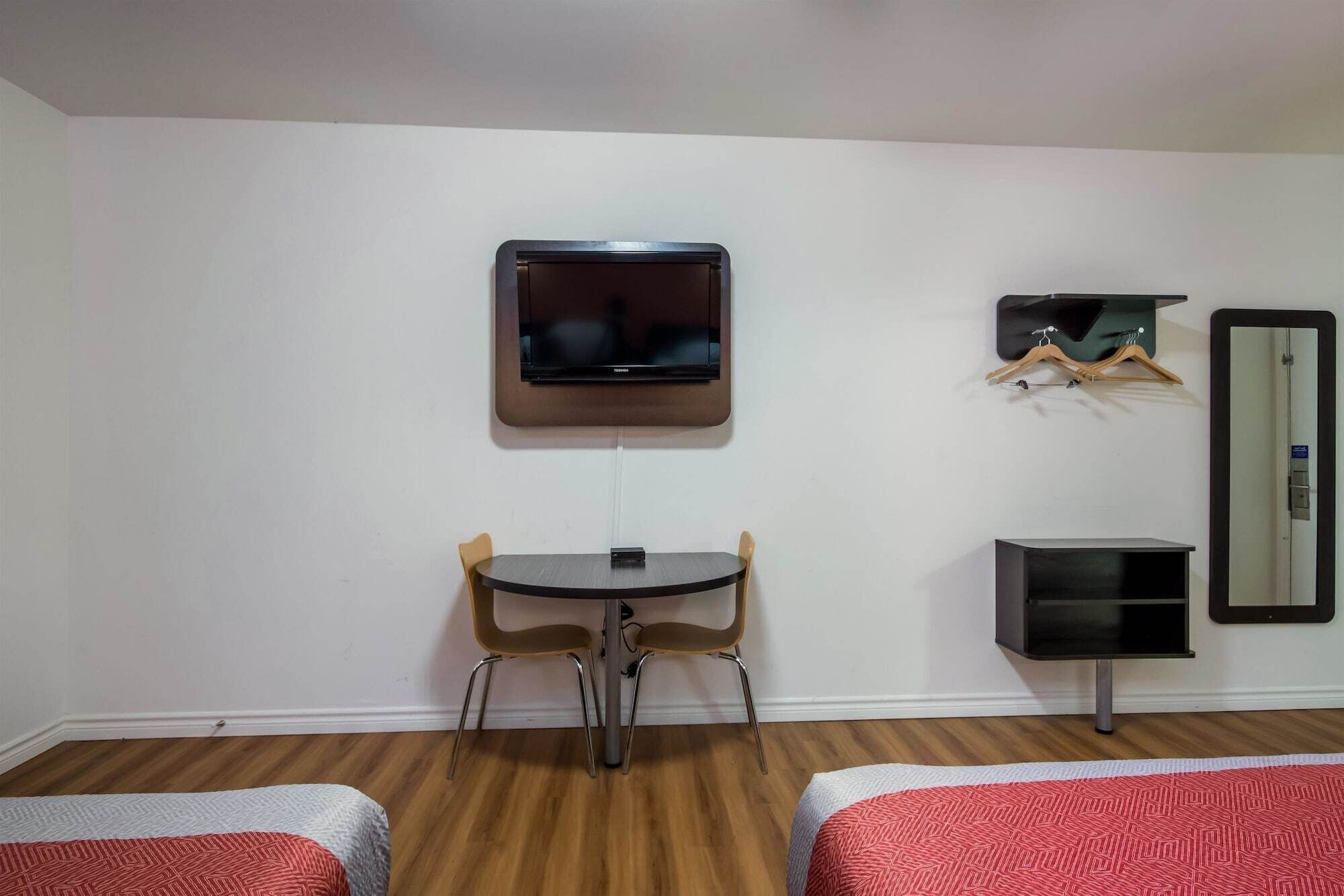 Una habitación pequeña con cama, escritorio, silla, televisor, espejo y perchero.