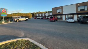 A parking lot with multiple cars, a motel sign, and a building with a modern design. - Motel 6 Sudbury, ON (Sudbury)