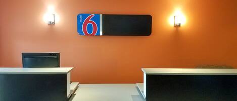 Een receptiebalie met een groot bord waarop kamer nummer 6 staat, twee wandlampen en een zwarte stoel.