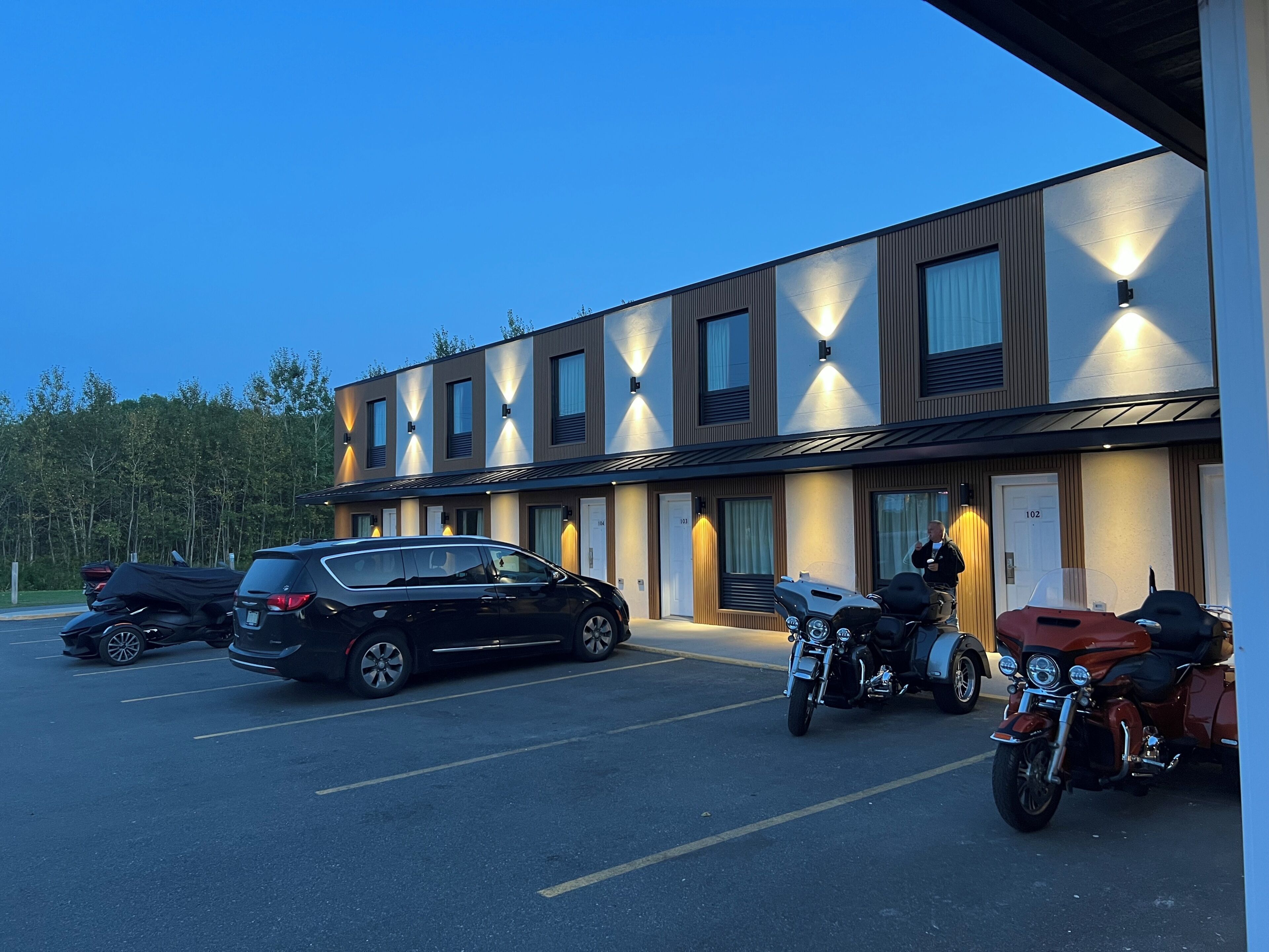 En moderne bygning med parkeringsplads, flere biler og motorcykler.