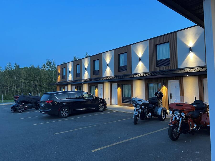 Un edificio moderno con un estacionamiento, varios autos estacionados y motocicletas.