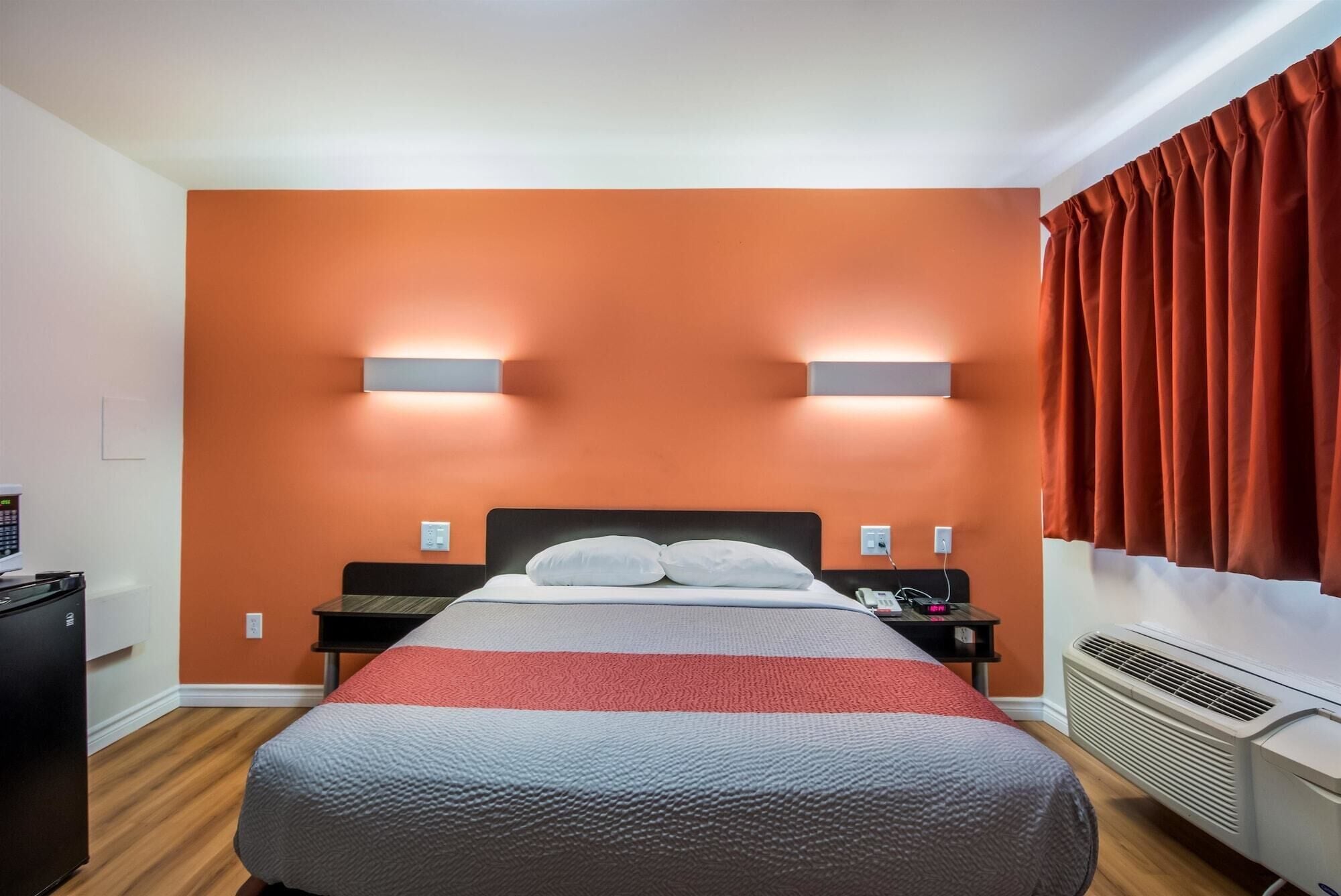 A hotel room with a bed, two bedside tables, a heater, and a wall-mounted light fixture.