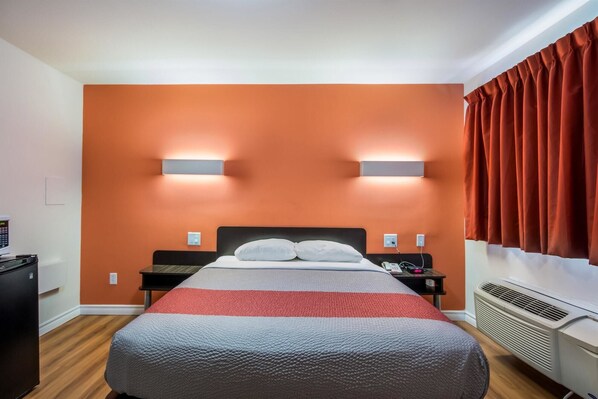 A hotel room with a bed, two bedside tables, a heater, and a wall-mounted light fixture. - Motel 6 Sudbury, ON (Sudbury)