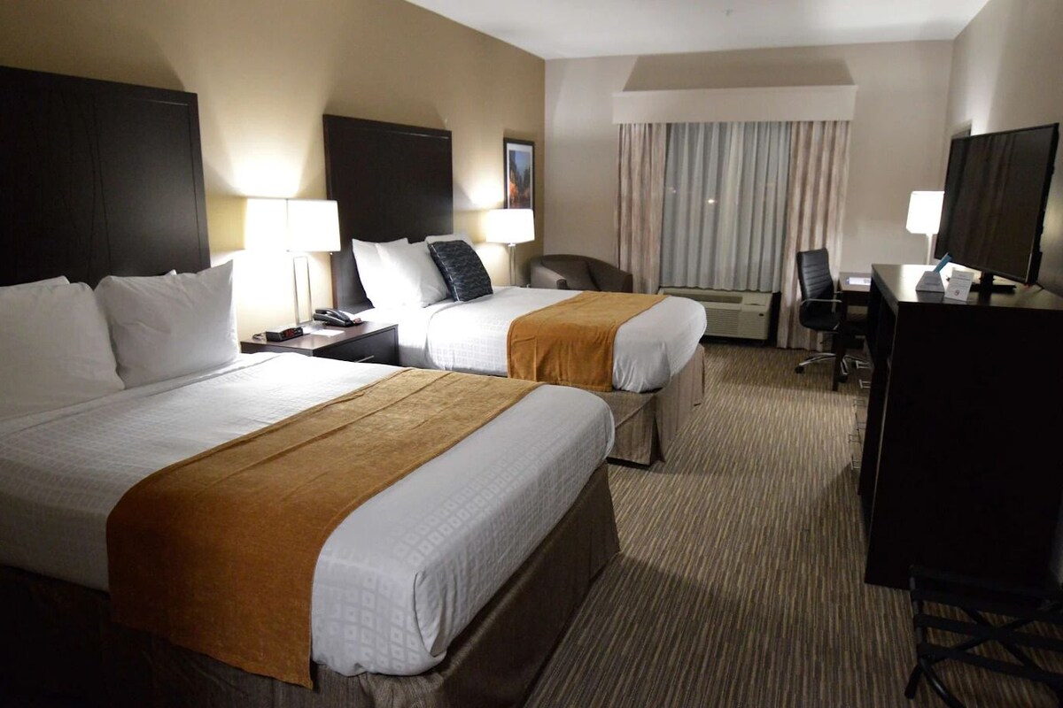 A hotel room with two beds, a desk, a chair, a TV, and a window with curtains.