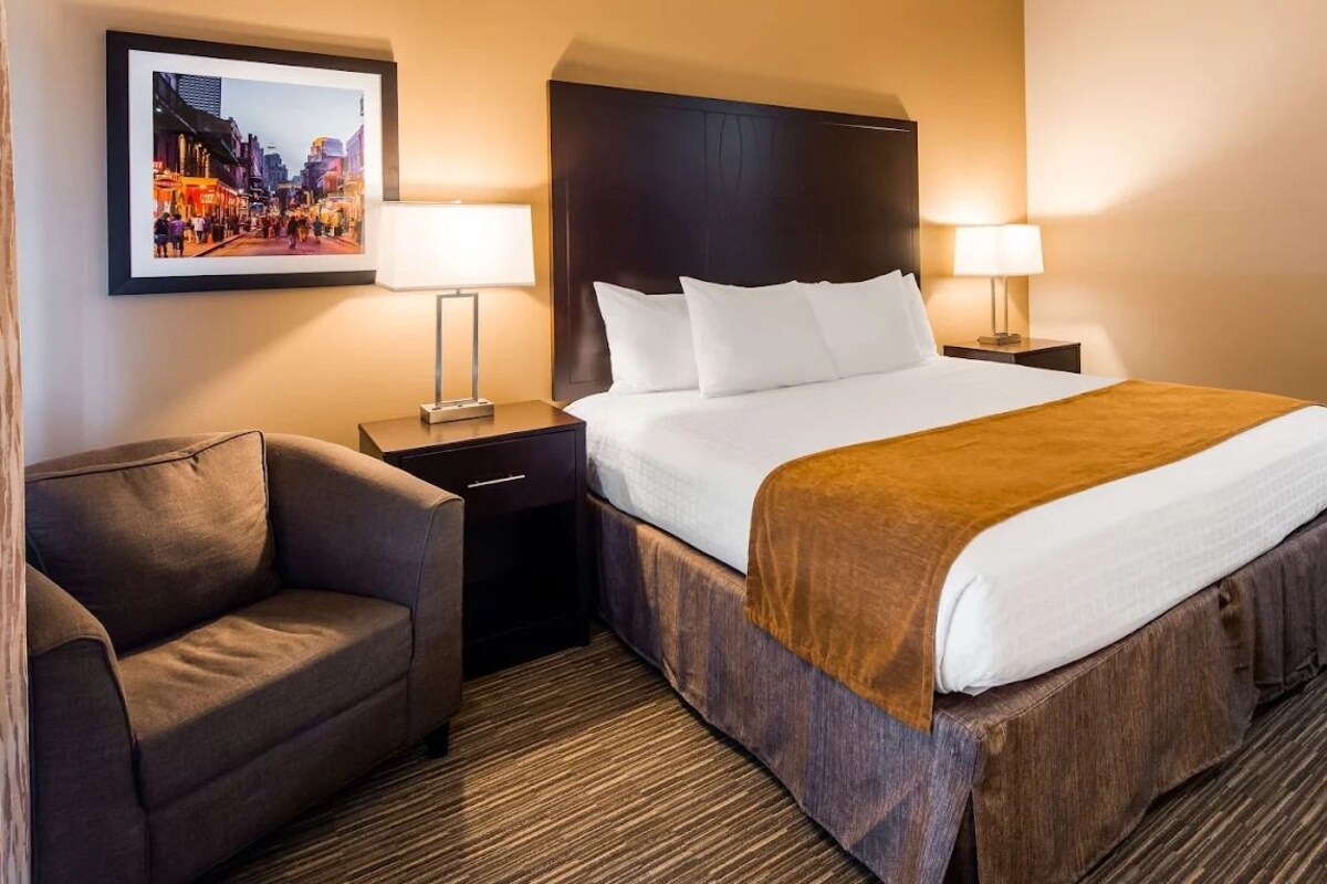 A hotel room with a bed, two bedside tables, a chair, a framed picture on the wall, and a carpeted floor.