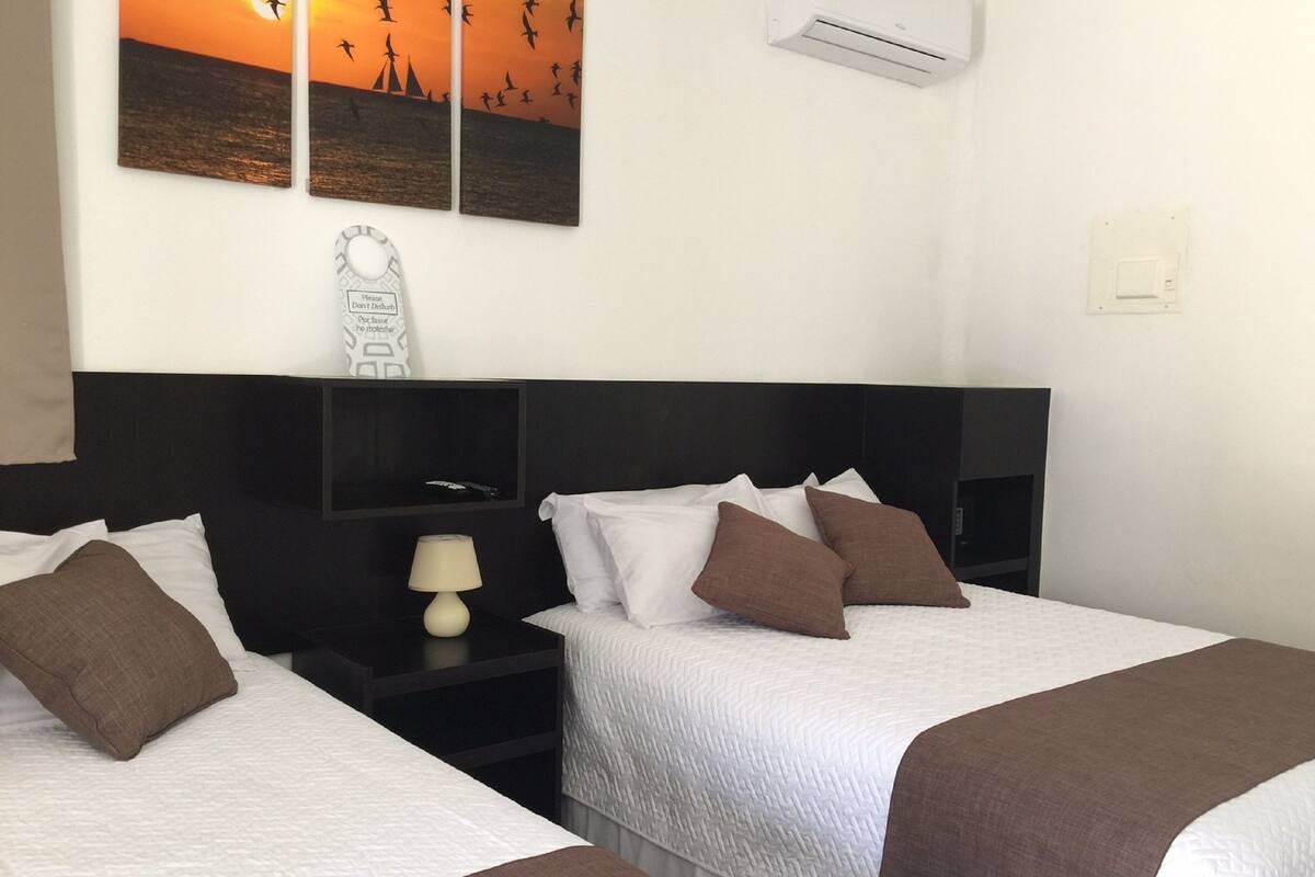 Ein Hotelzimmer mit zwei Betten, einem Nachttisch mit Lampe und Wandbild mit Sonnenuntergangsmotiv.