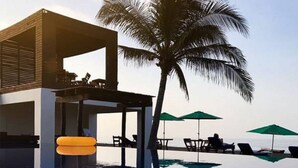 Een modern zwembadgedeelte met loungebedden en parasols, een palmboom en een gebouw met een glazen gevel.