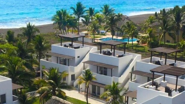 Een modern resort met meerdere witte gebouwen, een zwembad en uitzicht op het strand.
