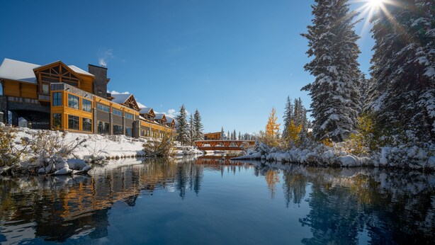 A snow-covered landscape with a reflective lake, wooden buildings, and snow-laden trees. - The Malcolm Hotel  (Canmore)