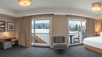 Ein Hotelzimmer mit einem großen Bett, einem Schreibtisch, einem Stuhl und einem Balkon mit Blick auf Bäume und Berge.