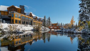 A lodge with a reflective pond, snow-covered trees, and a clear blue sky. - The Malcolm Hotel  (Canmore)