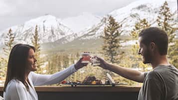 Um casal brindando com bebidas à mesa, com vista para a montanha.