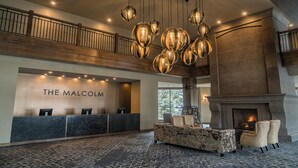 A reception area with a stone fireplace, a reception desk, and a seating area with a stone bench and chairs. - The Malcolm Hotel  (Canmore)