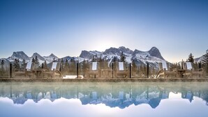 A pool with wooden lounge chairs and a mountain view. - The Malcolm Hotel  (Canmore)
