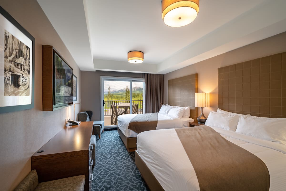 A hotel room with two beds, a desk, and a balcony with a view of mountains.