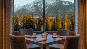 A dining area with a table set for four, overlooking a mountainous landscape through large windows. - The Malcolm Hotel  (Canmore)