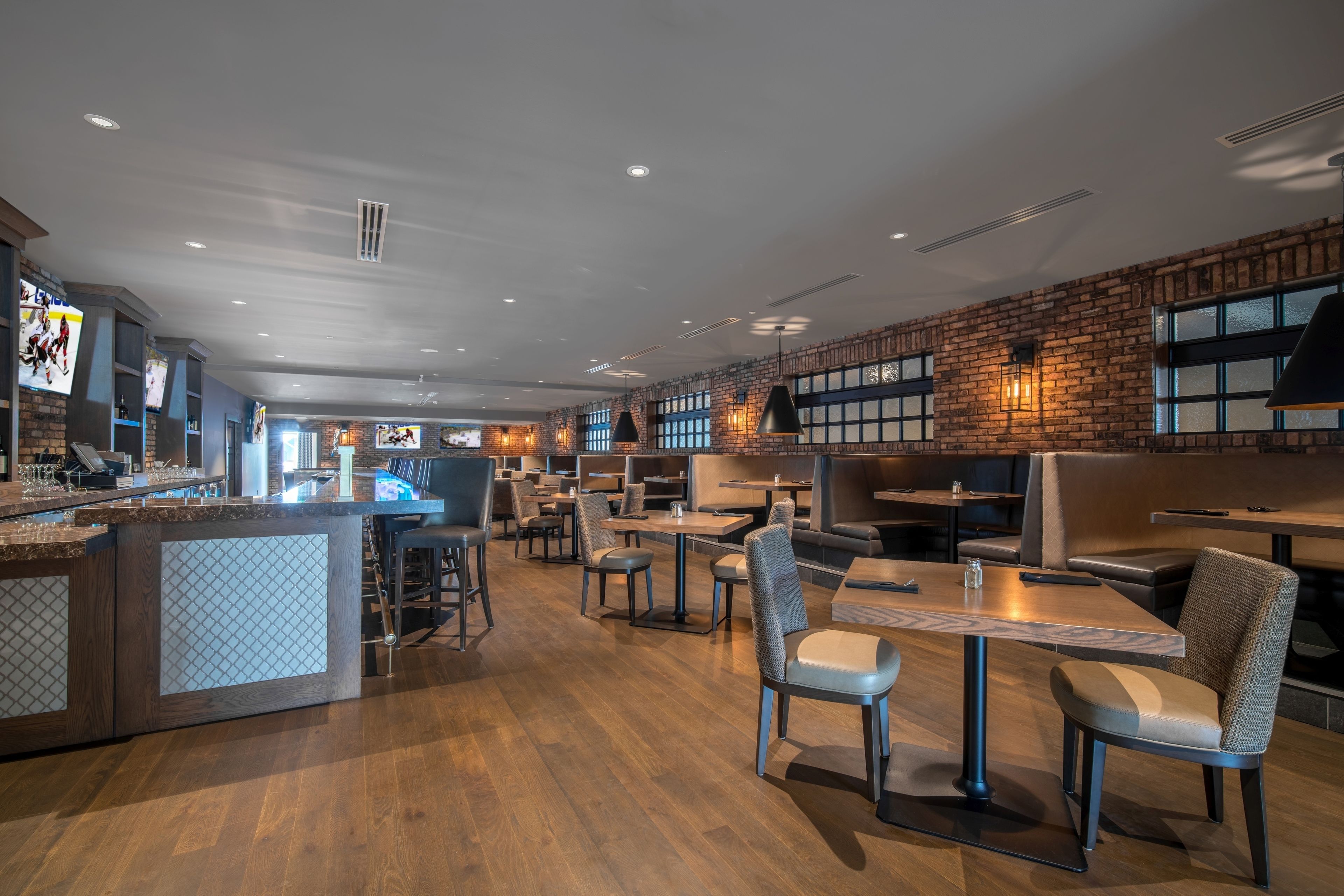 A modern restaurant with wooden flooring, brick walls, and a variety of seating options including booths and tables.