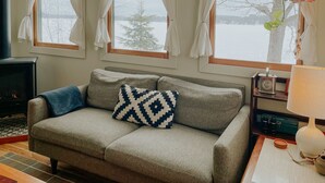 A cozy living room with a grey sofa, patterned cushions, and a window with curtains.