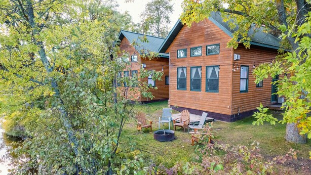 A cabin with a wooden exterior, a grassy yard, and a fire pit.
