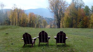 Three Adirondack chairs facing a forest with autumn foliage and mountains in the background. - Beautiful cottage on scenic Adirondack hobby farm  (North River)