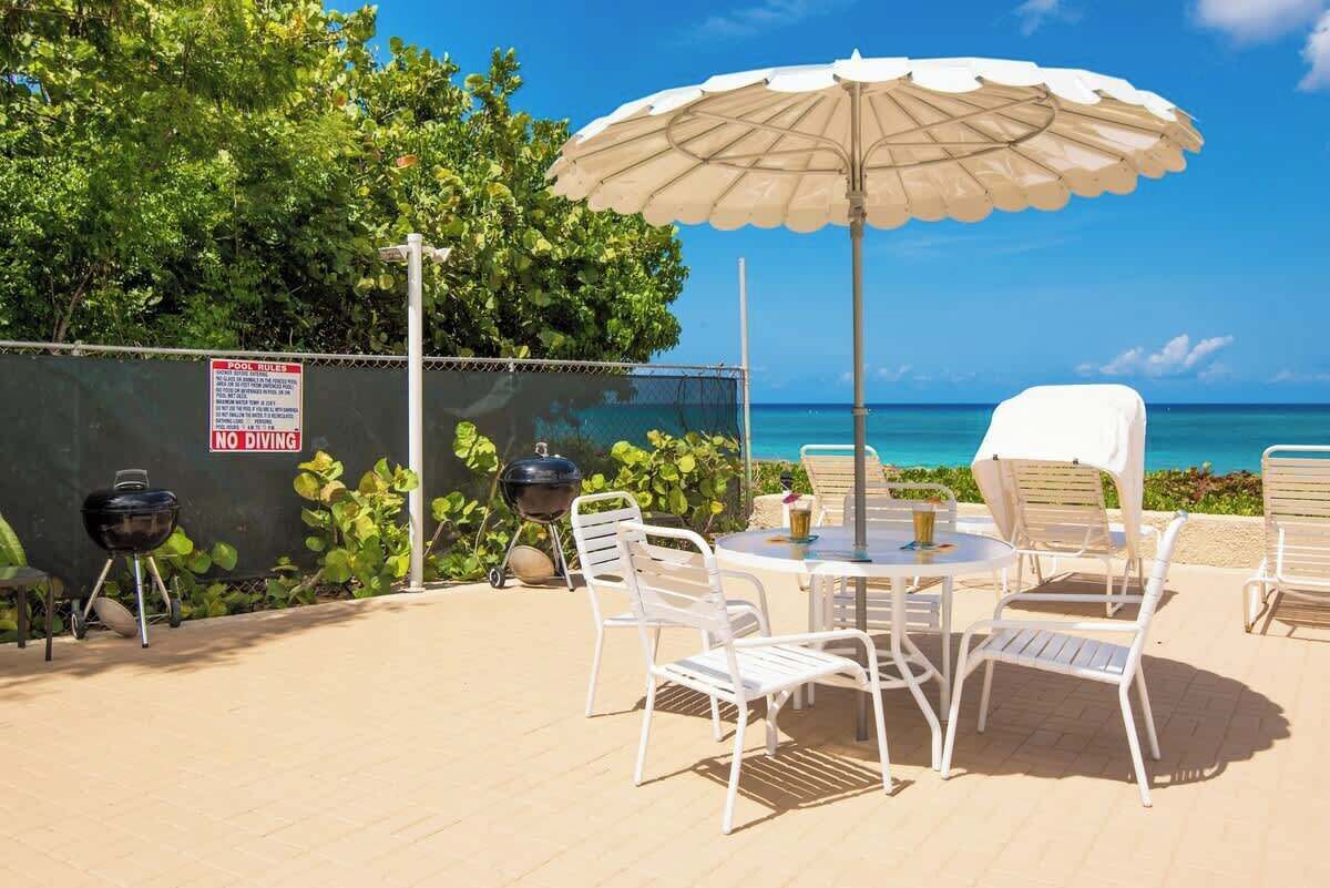 An outdoor patio with a table, chairs, a grill, and an umbrella.