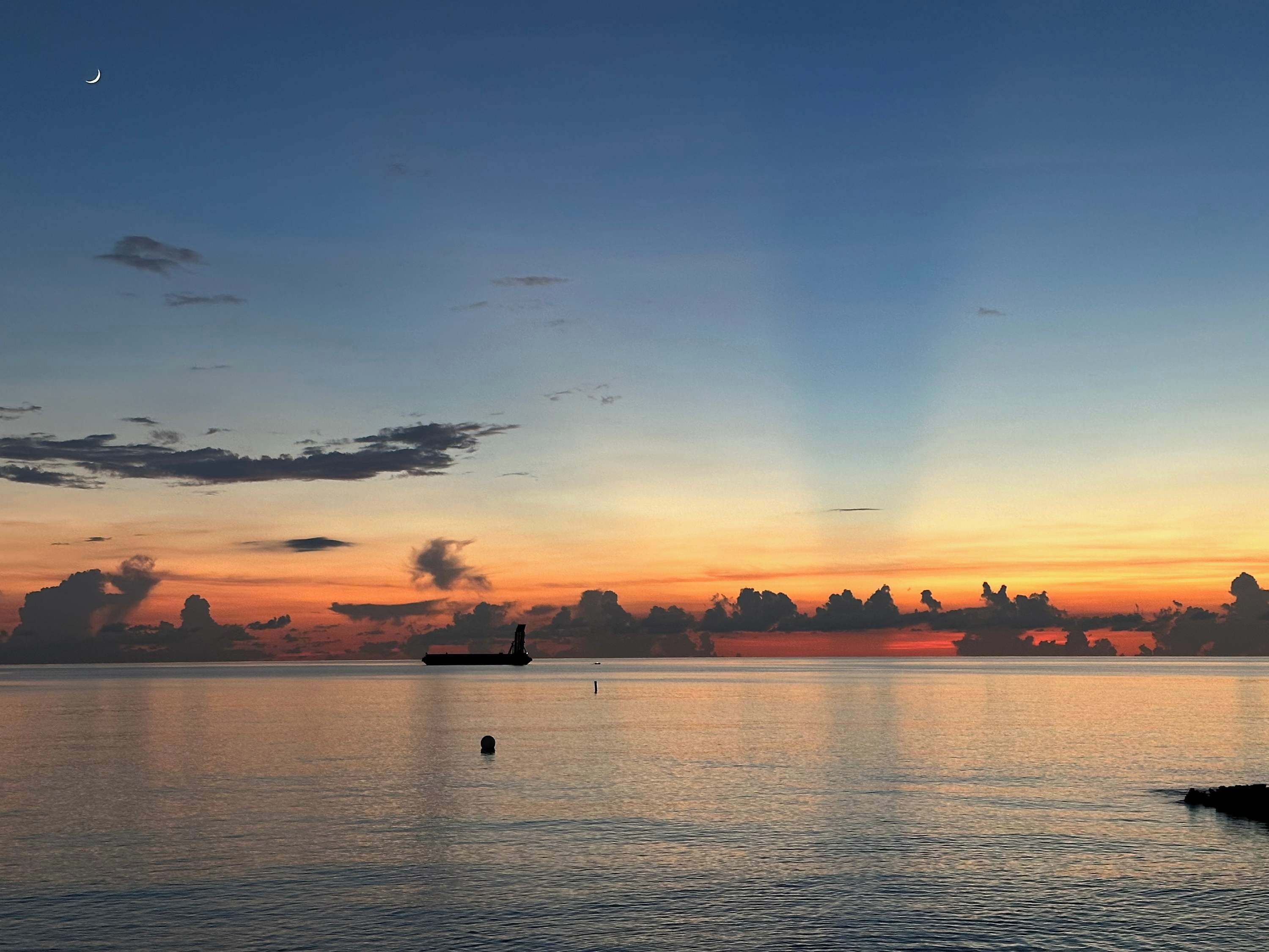 A calm body of water with a distant ship and a clear sky.