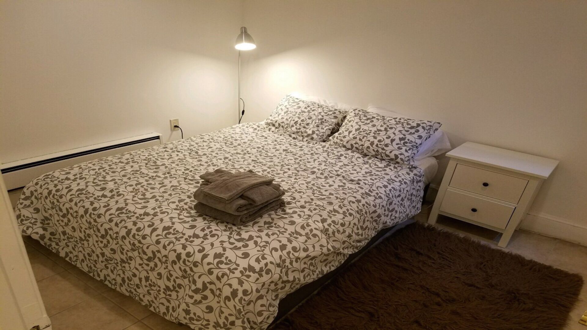 Een slaapkamer met een bed, een nachtkastje en een zacht tapijt.