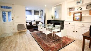 A modern living room with a glass dining table, white chairs, a red patterned rug, a fireplace, and a sofa with cushions. - Capitol Hill 2 Bedroom, 6ppl, Patio, Free Parking, near Capitol, Eastern Market (Washington)