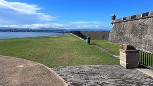A coastal fort with a grassy area, a paved walkway, and a view of the sea and distant mountains. - Walking distance to Old SJ, Cruise Ports & Beaches - WIFI - Queen size bed - (San Juan)
