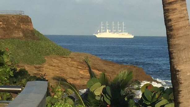 A coastal scene with a ship in the distance, rocky terrain, and palm trees. - Walking distance to Old SJ, Cruise Ports & Beaches - WIFI - Queen size bed - (San Juan)