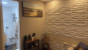 A modern bedroom with a bed, a wooden nightstand, a wall-mounted painting, and a textured wall design. - Walking distance to Old SJ, Cruise Ports & Beaches - WIFI - Queen size bed - (San Juan)