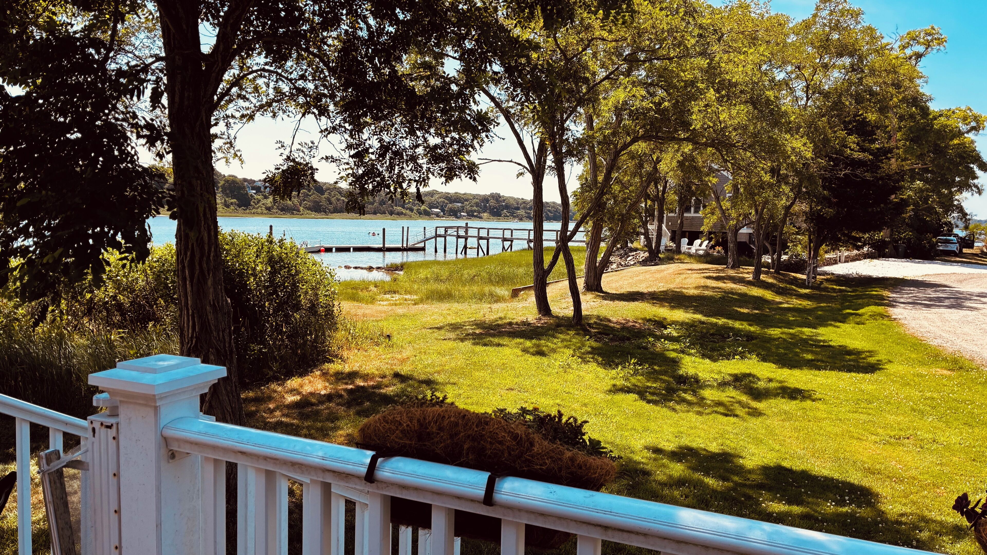 A grassy yard with a dock extending into a lake, surrounded by trees and a white fence.