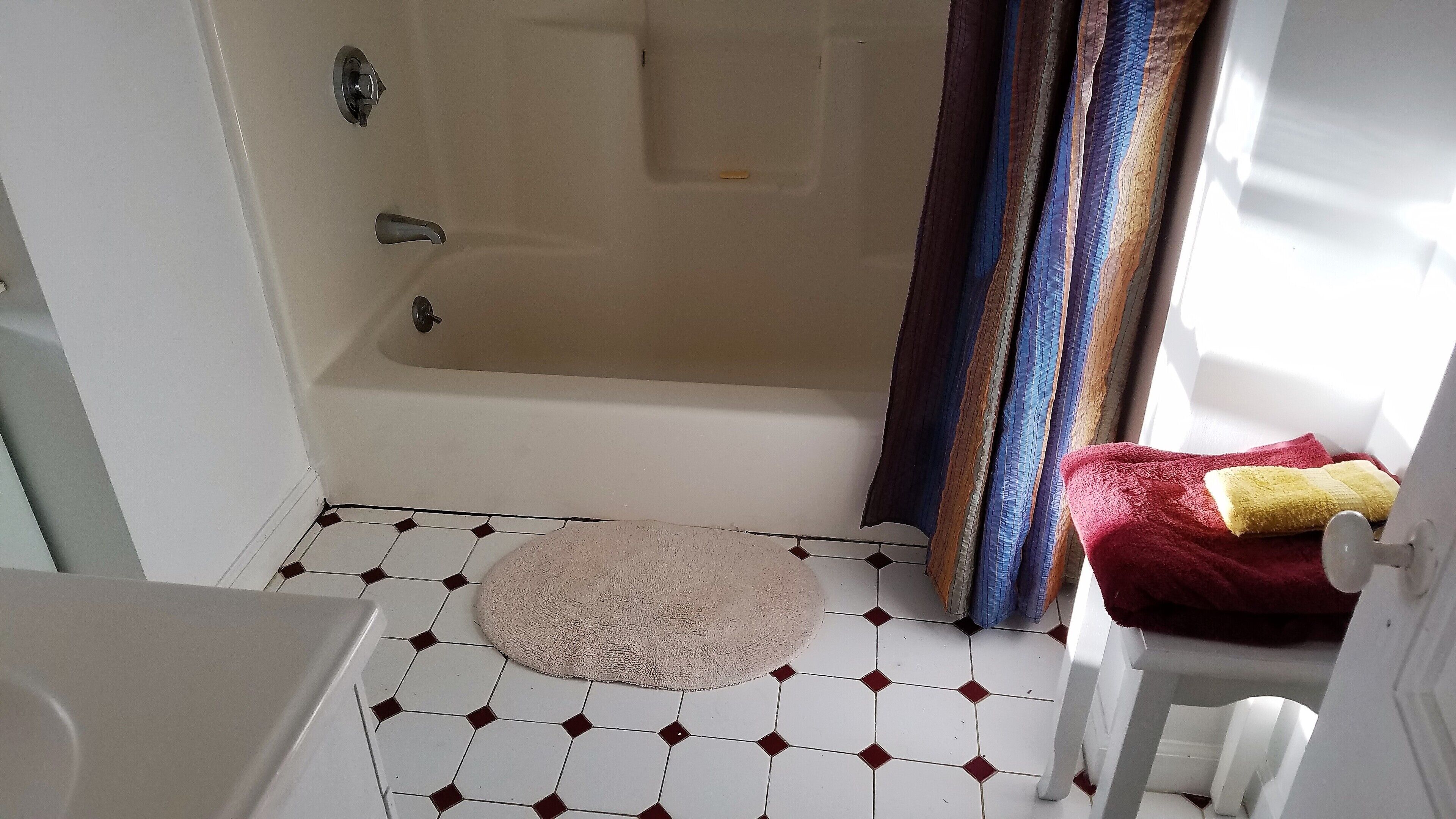 Une salle de bain avec une baignoire, une douche, des toilettes et un lavabo. On y trouve un porte-serviettes avec une serviette rouge et une serviette jaune.
