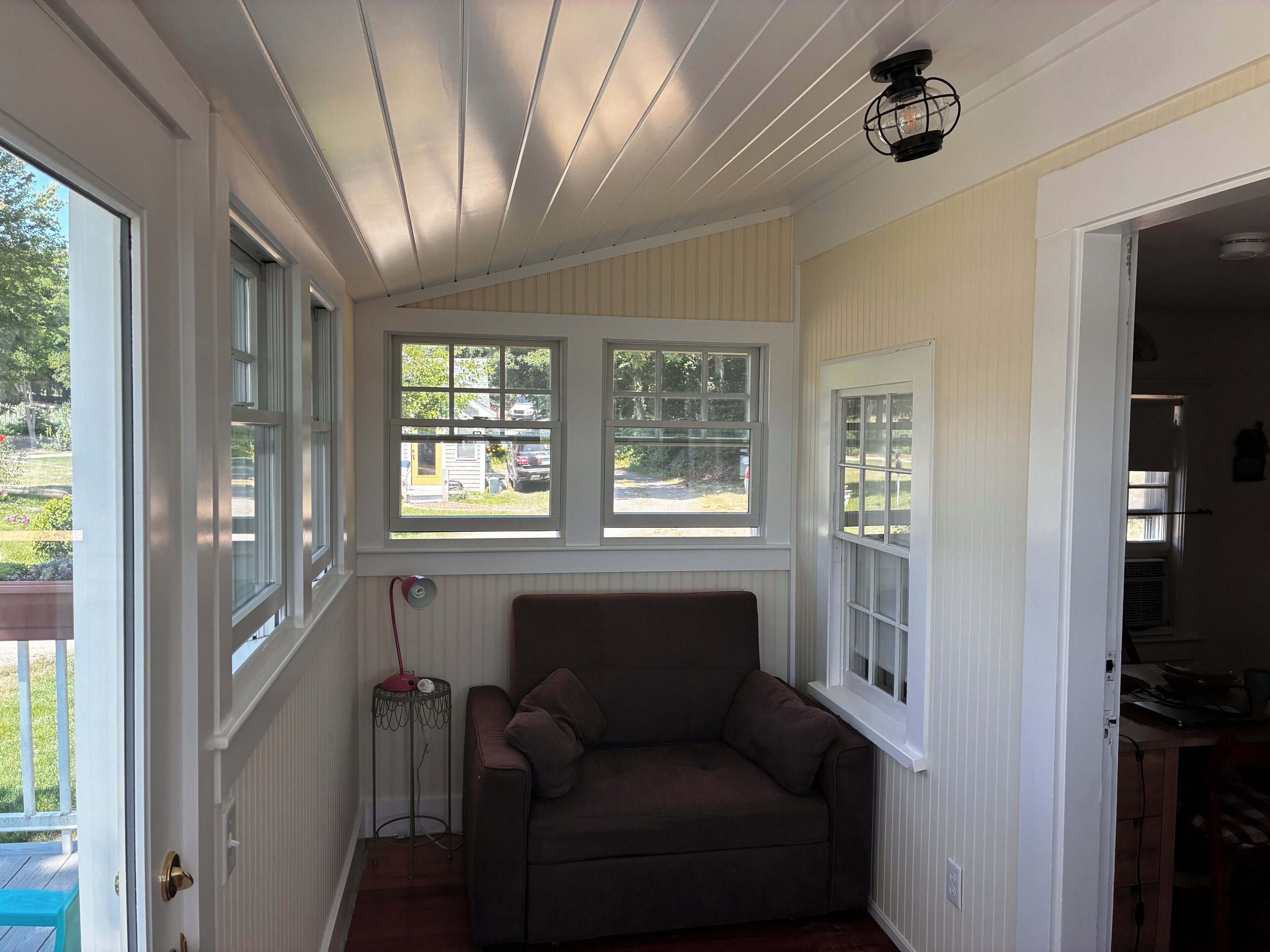 A room with a brown sofa, two windows, a ceiling light fixture, and a door leading to another room.