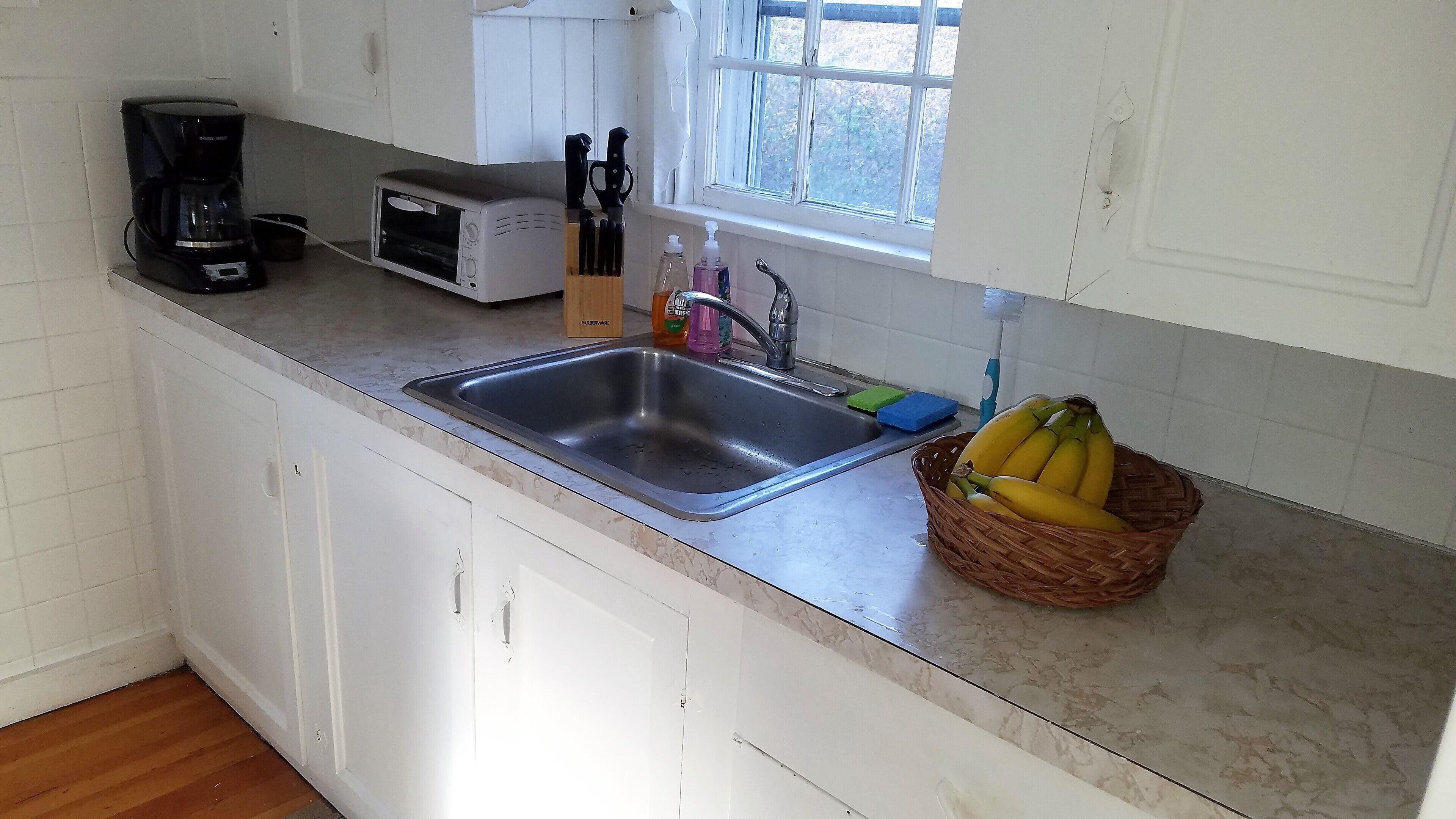 A kitchen with a sink, a toaster, a coffee maker, and a basket of bananas on the counter.
